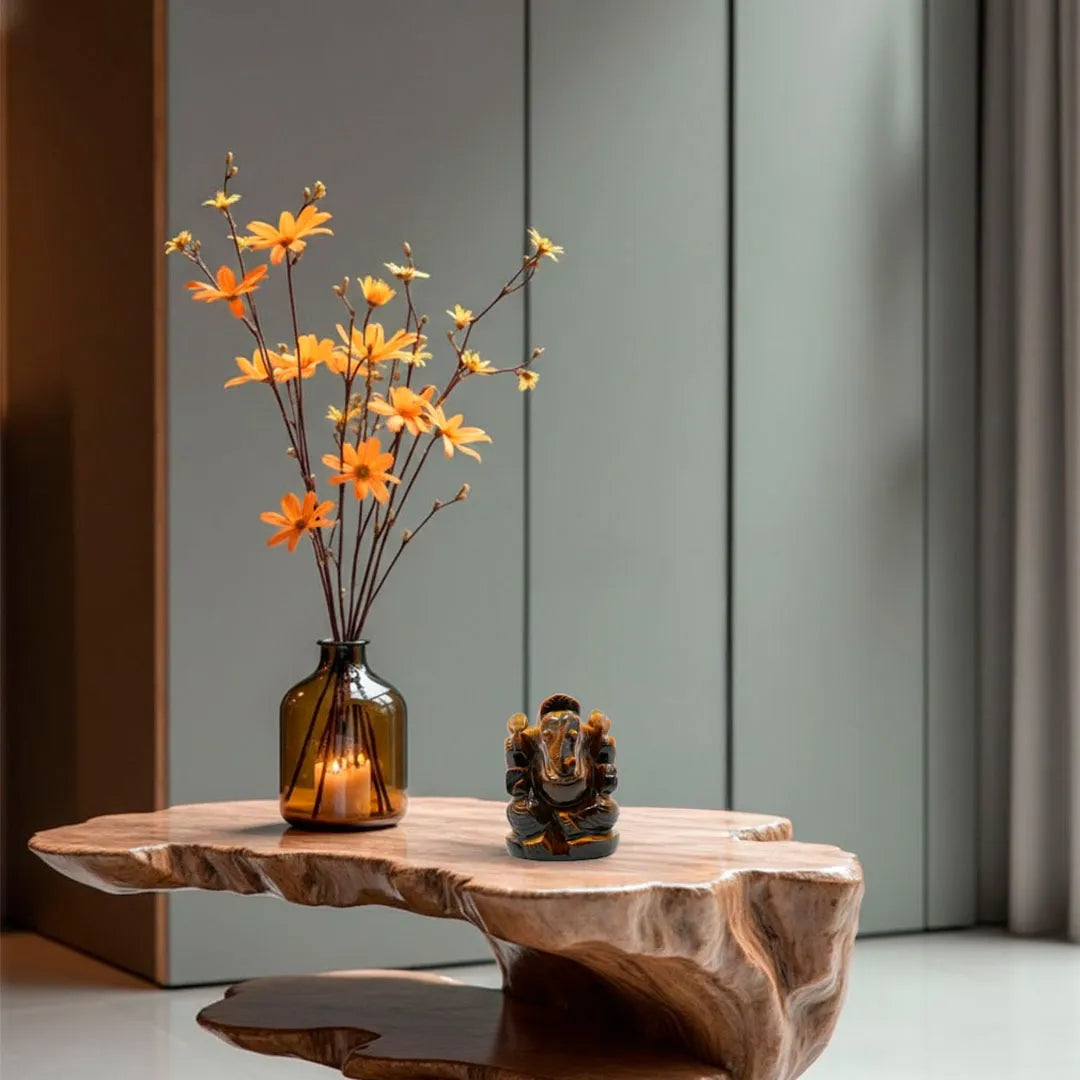 Decorative setup with a vase of orange flowers, a small statue, and a candle on a wooden table.