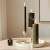 Three black candles with gold bases on a white tray against a neutral wall.