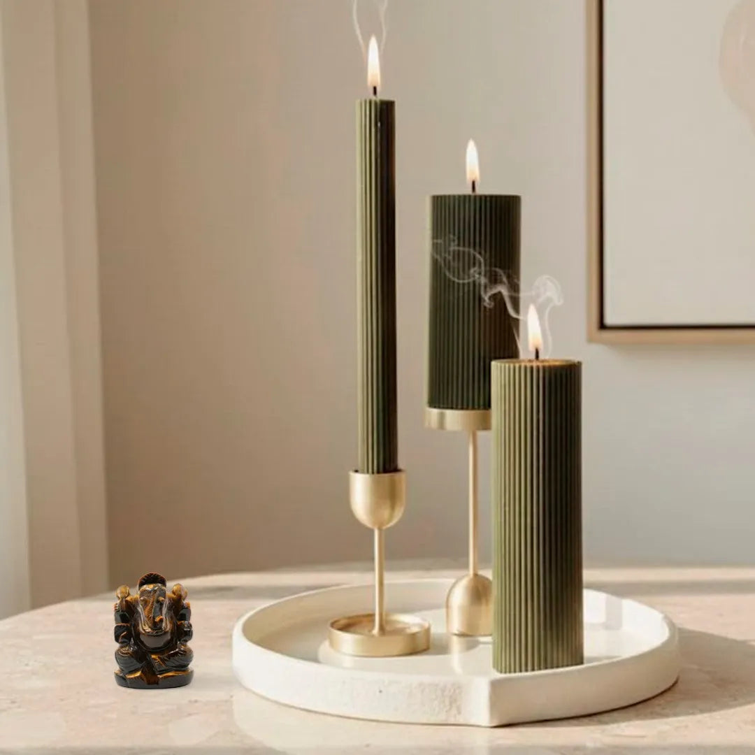 Three black candles with gold bases on a white tray against a neutral wall.