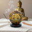Decorative tiger eye sphere with tree of life design in front of a Buddha statue