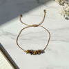 golden thread bracelet with tiger eye stone beads on a light marble surface with flowers