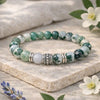 Green and white beaded bracelet on a stone surface with flowers