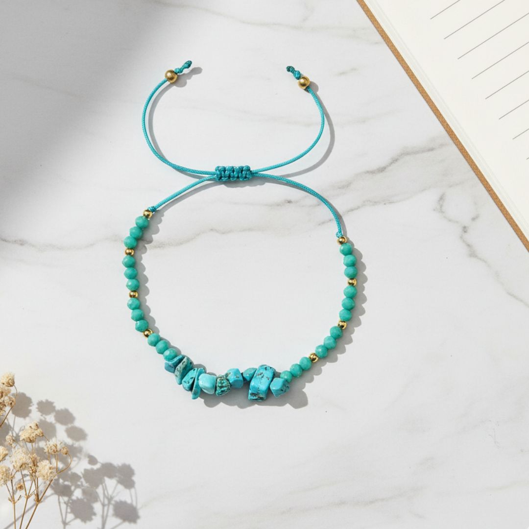 Turquoise beaded thread bracelet on a marble surface with a wooden stick and dried flowers.