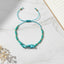 Turquoise beaded thread bracelet on a marble surface with a wooden stick and dried flowers.