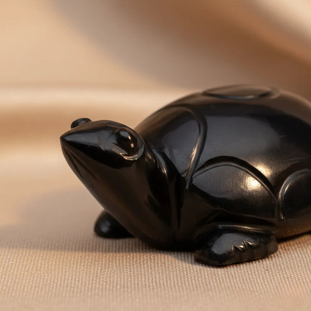 Black ceramic frog figurine on a beige fabric background