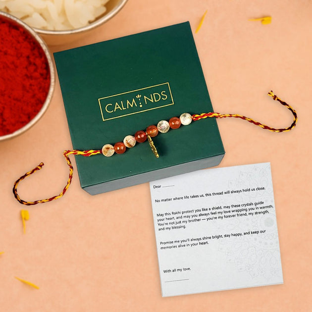 Crystal rakhi with a message card on a green box labeled 'Calminds' on a peach background.